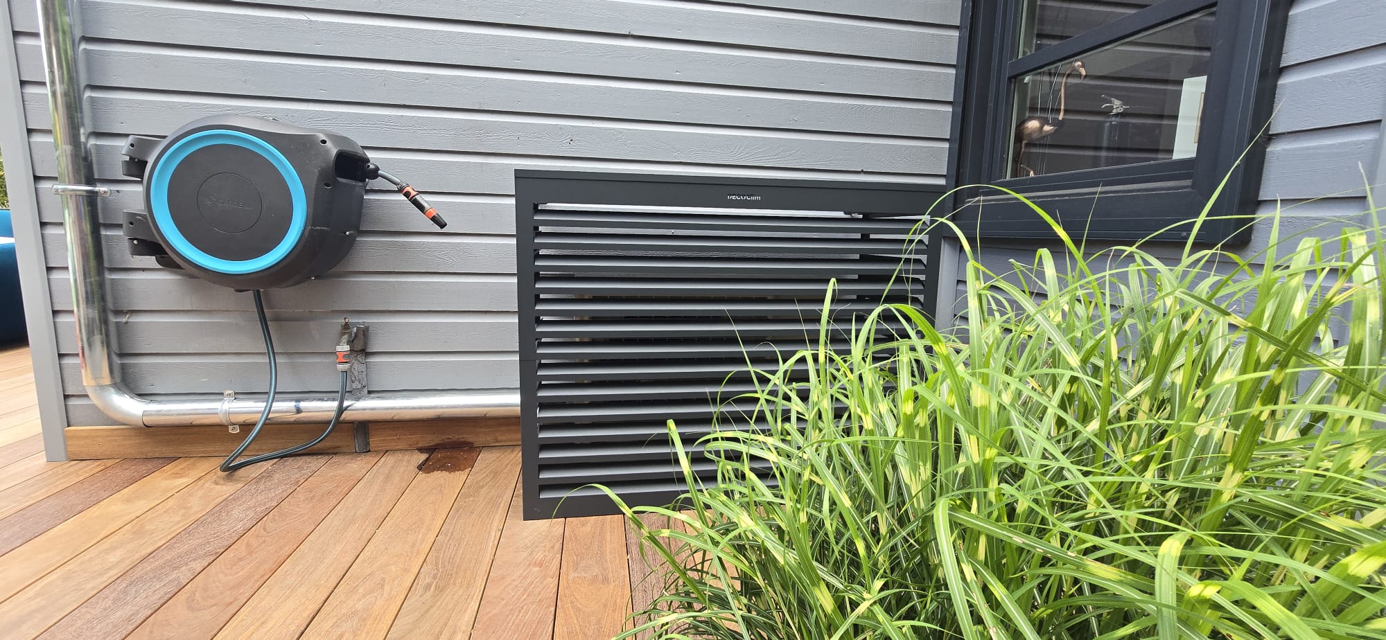 Cache climatisation aluminium gris anthracite habillant un groupe extérieur Daikin en façade, à proximité d'une terrasse en bois