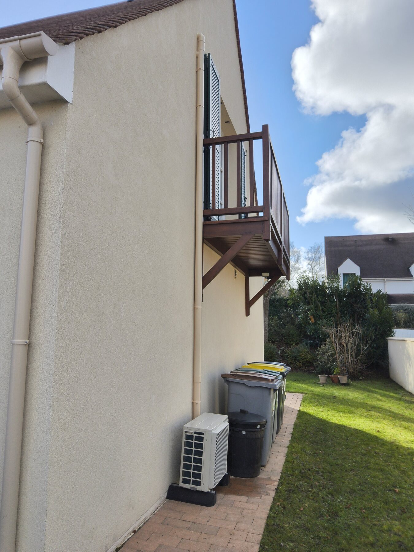 Groupe extérieur Daikin monosplit posé au sol sur socle en pignon d'une maison à Morainvilliers, liaisons frigorifiques dans une goulotte beige assortie à la façade